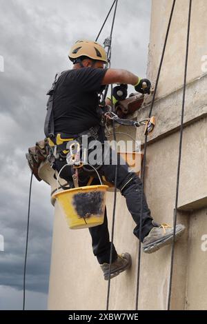 Akrobatik-Seilbau-Angestellter, der mitten in der Luft steht und an einer Fassade arbeitet. Stockfoto