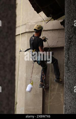 Akrobatik-Seilbau-Angestellter, der mitten in der Luft steht und an einer Fassade arbeitet. Stockfoto