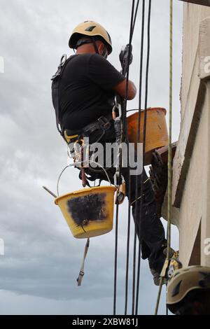 Akrobatik-Seilbau-Angestellter, der mitten in der Luft steht und an einer Fassade arbeitet. Stockfoto