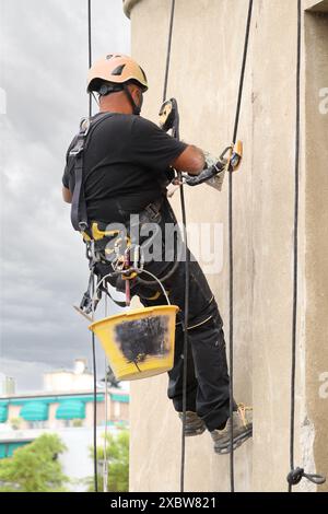 Akrobatik-Seilbau-Angestellter, der mitten in der Luft steht und an einer Fassade arbeitet. Stockfoto