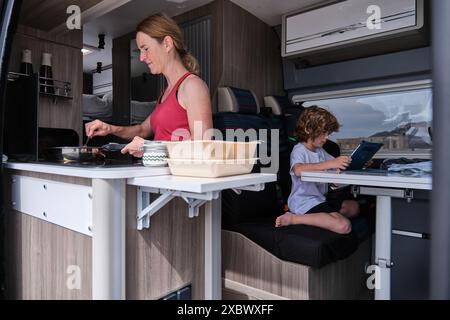 Eine Mutter kocht im Wohnmobil, während der Sohn mit einem digitalen Tablet spielt Stockfoto