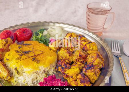 Gesundes und farbenfrohes nahöstliches Essen mit Hühnerkebab, Safranreis und Gemüse auf einer Platte neben einem Glas Wasser Stockfoto