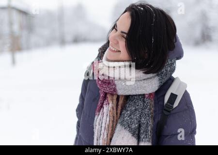 Junge lächelnde, schöne Frau, die draußen einen Schal trägt, während der Schnee fällt Stockfoto