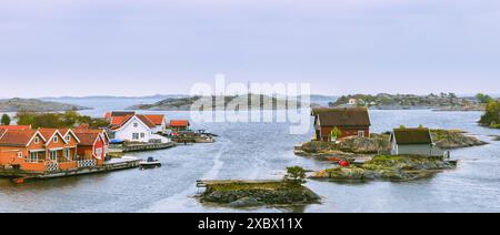 Bezaubernde rot-weiße Cottages am Ufer, mit Booten am Pier, Sommerhütten am Meer auf der Insel Flekkeroya. Kristiansand, Nein Stockfoto