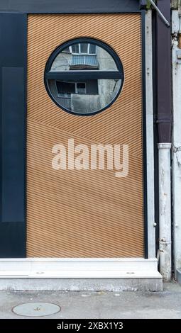 Alte helle Holztür mit Rahmen an der Außenfassade des Gebäudes an einer Straße, das runde Glasfenster Stockfoto