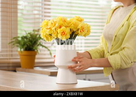 Weibliche Hände berühren Narzissen in der Vase in der Küche Stockfoto