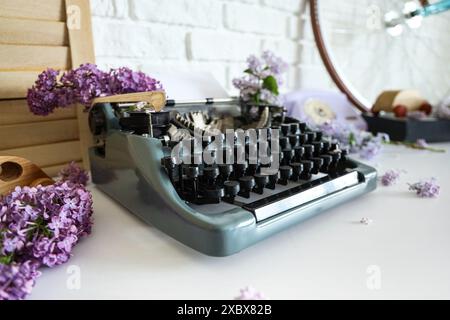 Vintage Schreibmaschine mit Fliederblumen auf dem Tisch im Büro des Autors, Großaufnahme Stockfoto