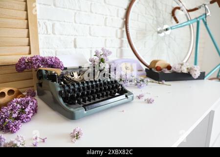 Vintage Schreibmaschine mit Fliederblumen auf dem Tisch im Büro des Autors, Großaufnahme Stockfoto