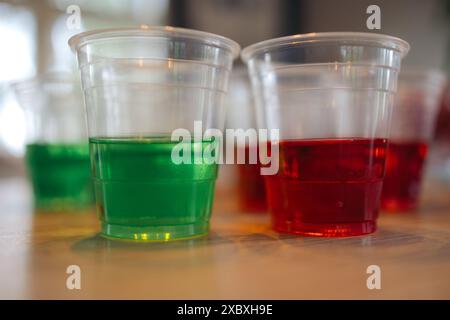 Zwei Tassen Gelee auf einem Holztisch - eine in grüner und eine in roter Farbe, gestapelt vor anderen Tassen Stockfoto