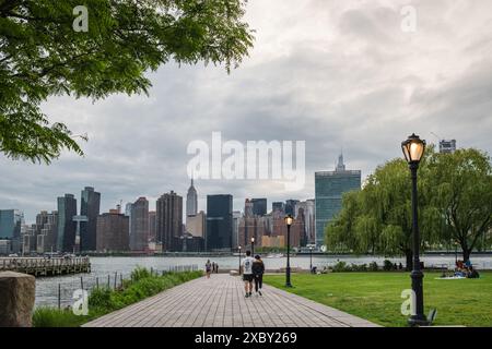 NEW YORK CITY - 17. MAI 2024: Touristen und Einheimische genießen im Gantry Plaza State Park in Long Island City einen warmen Sonnenuntergang im Frühling Stockfoto