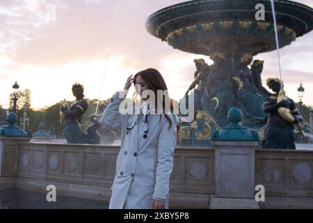 Das schöne Mädchen steht bei Sonnenuntergang auf einem Platz in Paris im Frühling an einem Brunnen Stockfoto