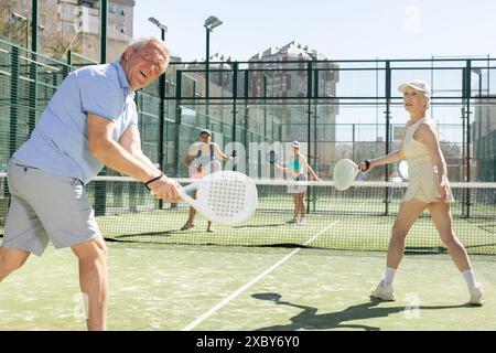 Reifes, sportliches, reifes Ehepaar, das am sonnigen Tag auf dem Hof Padel spielt Stockfoto