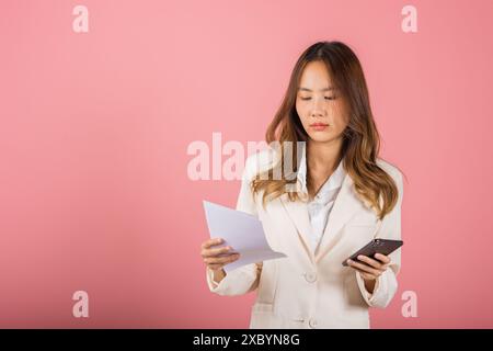 Porträt einer asiatischen jungen Frau mit Papier, die Rechnungen zur Hand und Handy zur Bezahlung berechnet Stockfoto