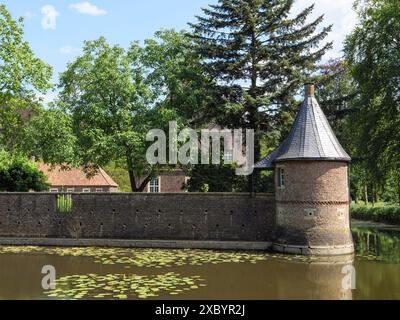 Runder Backsteinturm mit spitzem Dach von einem Graben, umgeben von Sommerbäumen und schöner Natur, ochtrup, münsterland, deutschland Stockfoto