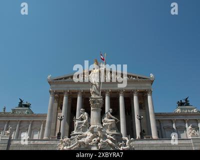 Ein weitläufiger Blick auf ein Gebäude mit Säulen und einer Statue von Pallas Athena im Zentrum unter blauem Himmel, Wien, Österreich Stockfoto