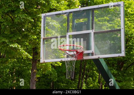 Basketballkorb im Freien mit rotem Rand und Kettennetz vor einem Hintergrund von grünen Bäumen und blauem Himmel Stockfoto
