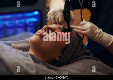 Frau bekommt Rotlichttherapie und Gesichtsmassage im Schönheitssalon Stockfoto