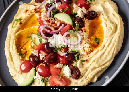 Griechischer Hummus mit frischen Gurken, Oliven, Tomaten, Fetakäse, roten Zwiebeln und Thymian auf grauem Teller, Nahaufnahme Stockfoto