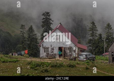 Eine Frau macht Hausarbeit in einem authentischen Hochland-Dorf. Ein armes Haus vor dem Hintergrund von Wolken, die die Berggipfel bedecken. Stockfoto