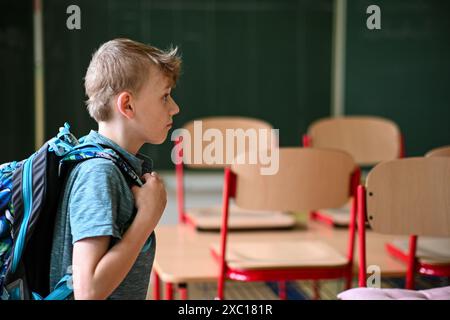 Schuljunge mit Rucksack, der im Klassenzimmer neben leeren Schreibtischen von der Kamera wegschaut Stockfoto