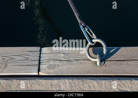 Festmacherring für Boote im Hafen mit Karabiner und schwarzem Seil vom Boot, Holzpier, sonniges Licht, Seilverbindung, Finnland Stockfoto