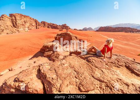 Einsamer Reisender sitzt inmitten der majestätischen Landschaften der Wüste Wadi Rum in Jordanien und spiegelt sich in der Einsamkeit vor dem riesigen, roten Sand und der Höhe wider Stockfoto