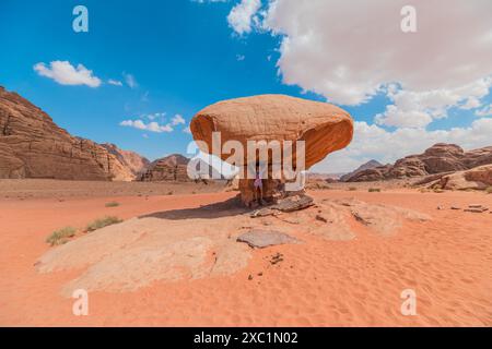 Die Touristenfrau steht unter dem berühmten Mushroom Rock in der Wüste Wadi Rum in Jordanien und zeigt die Schönheit und Größe der natürlichen Sandsteinformation Stockfoto