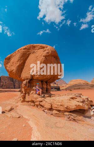 Die Touristenfrau steht unter dem berühmten Mushroom Rock in der Wüste Wadi Rum in Jordanien und zeigt die Schönheit und Größe der natürlichen Sandsteinformation Stockfoto