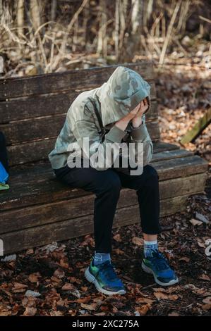 Teenager, der auf einer Bank im Wald sitzt, mit dem Kopf in den Händen Stockfoto