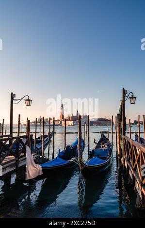 Angedockte überdachte Gondeln mit Kirche im Hintergrund in Venedig, Italien. Stockfoto