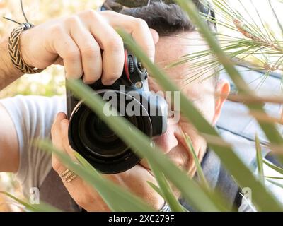 Nahaufnahme eines professionellen Fotografen, der hinter Blättern Fotos macht Stockfoto