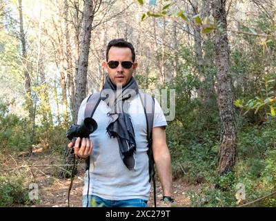 Mann, der auf dem Wald steht und eine Kamera hält, während er in die Kamera schaut Stockfoto