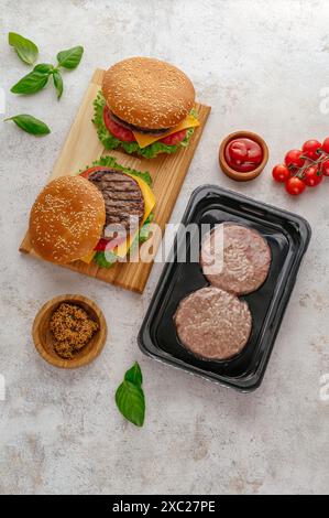Ein fertiger Burger und frische, rohe Burger-Patties daneben Stockfoto