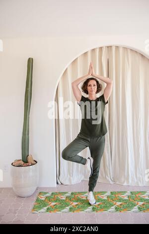 Frauen üben Yoga zu Hause mit Kakteen neben ihr Stockfoto
