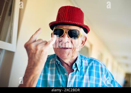 Rocker, Lächeln und Sonnenbrille mit Seniorenmann im Flur des Altersheims für eine gute Party am Wochenende. Porträt, lustig und Brille mit Happy Reife Stockfoto