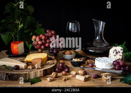 Tisch mit verschiedenen Käsesorten, Trauben, Glas und Karaffe mit Rotwein Stockfoto