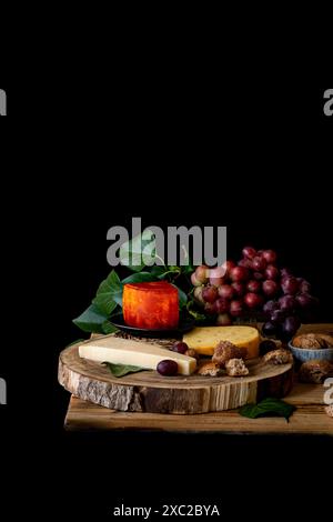 Tisch mit verschiedenen Käsesorten, Trauben, Brot und Nüssen, schwarzer Hintergrund Stockfoto