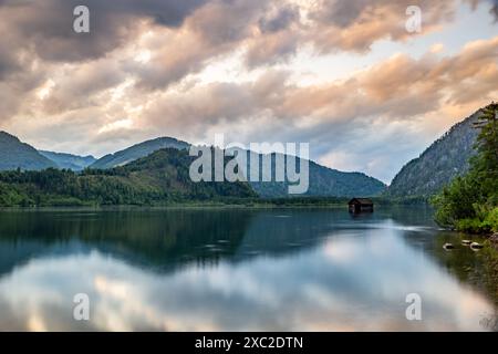 Eine malerische Szene am Almsee in Österreich, mit einem ruhigen See, der einen goldenen Sonnenuntergang reflektiert, mit einer kleinen Hütte im Wasser, die hoch aufragt Stockfoto
