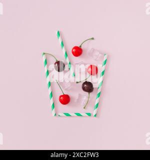 Kreatives Layout aus roten Kirschen, Eiswürfeln und Trinkstroh auf hellrosa Hintergrund. Minimales Cocktailkonzept. Sommergetränk-Komposition. Stockfoto