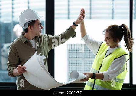 Zwei Ingenieure arbeiten an einem Projekt zusammen, überprüfen den Entwurf und feiern den Erfolg in einem modernen Büroumfeld mit natürlichem Licht Stockfoto