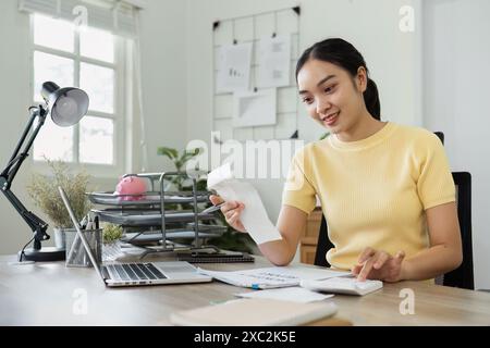 Junge Frau, die Finanzen am Home Office Desk mit Laptop, Rechnungen und Dokumenten verwaltet, Konzept der Finanzplanung und Budgetierung in einem modernen Zuhause Stockfoto