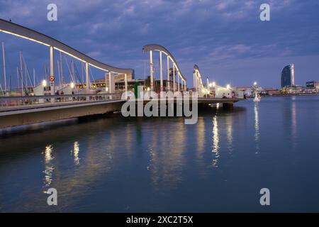 BARCELONA, SPANIEN. August 2022. Eine Brücke überspannt ein Gewässer mit einer Skyline der Stadt im Hintergrund. Die Brücke ist nachts beleuchtet, was einen Brückenschlag schafft Stockfoto