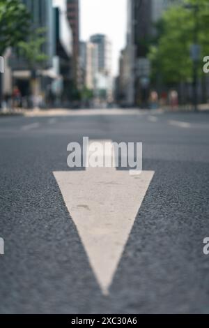 Nahaufnahme eines weißen Richtpfeils auf einer leeren Stadtstraße mit Gebäuden im unscharfen Hintergrund. Stockfoto