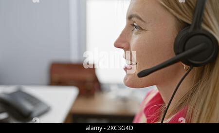 Profil einer lächelnden jungen Frau, die in einem Büro ein Headset trägt und einen Kundenservice anbietet. Stockfoto