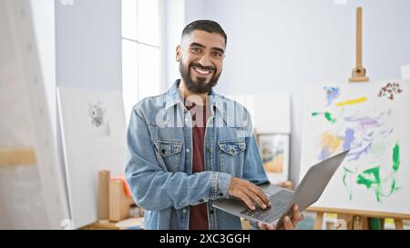 Ein gutaussehender bärtiger Mann mit Laptop in einem modernen Kunststudio, der Kreativität und Produktivität ausstrahlt. Stockfoto