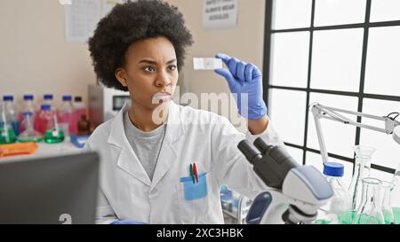 Eine fokussierte afroamerikanische Wissenschaftlerin analysiert einen Objektträger im Labor und demonstriert dabei Fachwissen und Präzision. Stockfoto