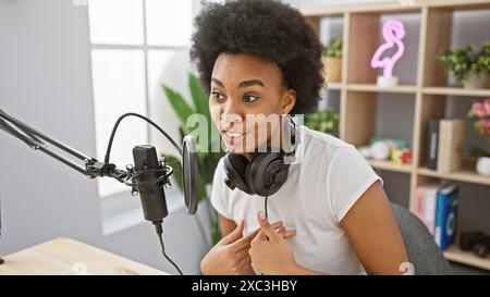 afroamerikanerin moderiert einen Podcast in einem modernen Radiostudio, trägt Kopfhörer und spricht in ein Mikrofon. Stockfoto