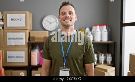 Hübscher junger Mann mit Bart, lächelt in die Kamera, trägt ein Schlüsselband und steht in einem Lagerhaus voller Spendenboxen. Stockfoto