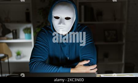 Geheimnisvolle Person in Maske, die nachts im Zimmer sitzt und Spannung weckt. Stockfoto