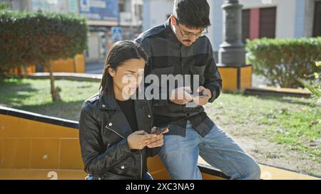 Ein Mann und eine Frau konzentrierten sich auf Smartphones, während sie zusammen auf einer Bank in einer sonnigen städtischen Umgebung saßen Stockfoto